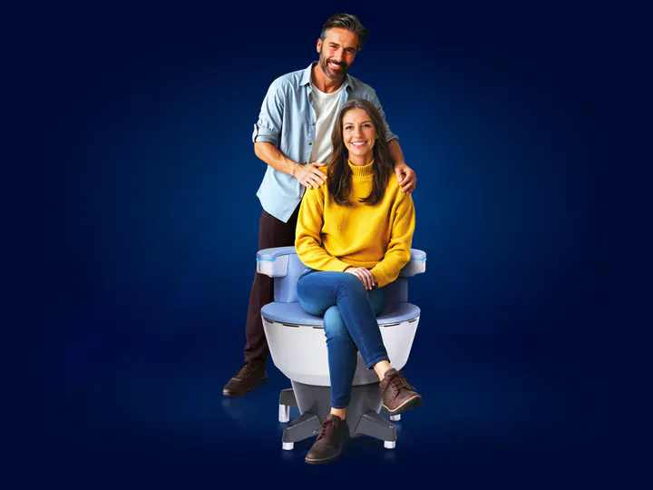 Woman seated fully clothed on an EMSELLA chair with a man standing behind her